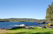 Udendørs udsigt over søen ved et sommerhus i Sunnemo, Sverige, med borde, bådebro og blå himmel.