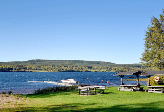 Vista lago da chalet a Sunnemo, Svezia, con tavoli da picnic, pontile, barca e colline boschive.