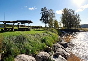 Sonniger Tag am Wasser bei einem 7-Personen-Ferienhaus in Sunnemo, Schweden, mit Bänken und Bäumen.