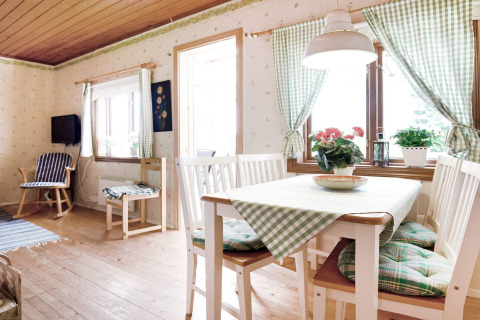 Coin repas lumineux dans un chalet pour 7 personnes à Sunnemo, Suède, avec rideaux à carreaux verts et bois.