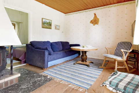 Salon confortable de chalet avec canapé bleu, table ronde, tapis rayé et plafond bois à Sunnemo, Suède.