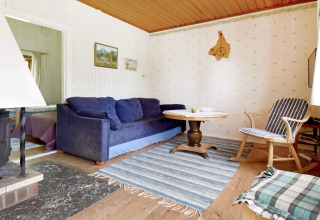 Soggiorno accogliente in chalet con divano blu, tavolo rotondo e tappeto a righe a Sunnemo, Svezia.