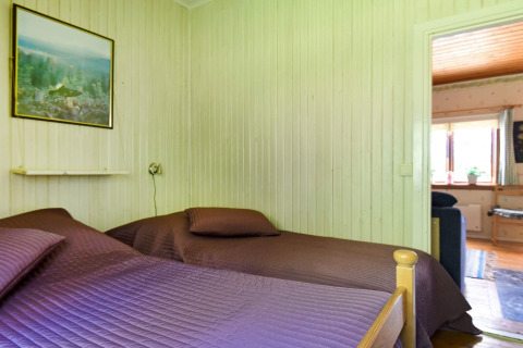 Soveværelse med to senge, lilla sengetæpper, vægmaleri og udsigt ind i stue i chalet i Sunnemo, Sverige.