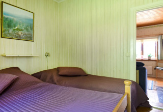 Soveværelse med to senge, lilla sengetæpper, vægmaleri og udsigt ind i stue i chalet i Sunnemo, Sverige.