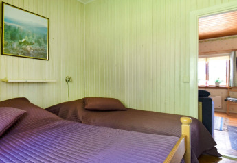 Slaapkamer met twee bedden, paarse spreien, schilderij en doorkijk naar woonkamer in chalet in Sunnemo, Zweden.