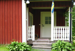 Porche d’un chalet avec drapeau suédois, panneaux rouges et blancs et plantes vertes à Sunnemo, Suède.
