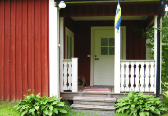 Front porch of a chalet with Swedish flag, red and white wooden panels, and green plants in Sunnemo, Sweden.