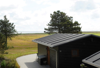 View of nature and water from Seaside Escape in Ho Bay, Denmark, with a black cabin and green trees.