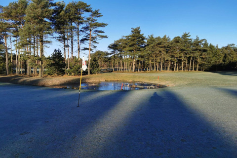 Golfbane nær hytten 'Seaside Escape in Ho Bay', Danmark, med frost på jorden og en lille dam.