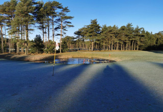 Golfbaan bij het huisje 'Seaside Escape in Ho Bay', Denemarken, met rijp en een kleine vijver zichtbaar.