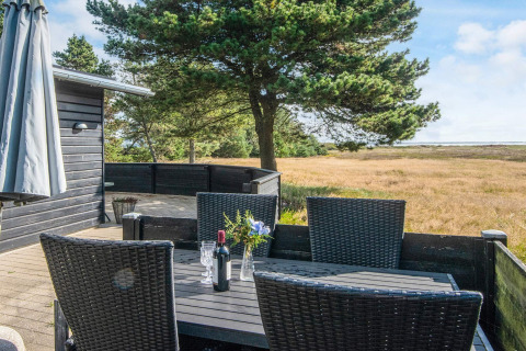 Terrasse bei 'Seaside Escape in Ho Bay', Dänemark, mit schwarzem Tisch, Stühlen und schöner Naturkulisse.