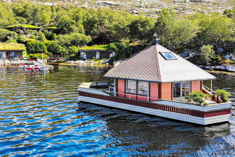 Houseboat 38507-SJØSTJERNEN floating on a lake, surrounded by trees and hills on a bright sunny day.