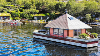 Houseboat 38507-SJØSTJERNEN floating on a lake, surrounded by trees and hills on a bright sunny day.