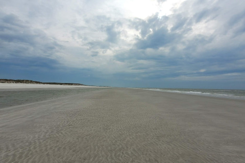 Grande plage de sable à Ho Bay au Danemark, sous un ciel nuageux, avec des vagues douces et horizon calme.