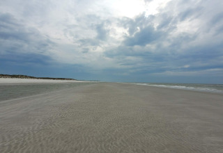 Brede zandstrand bij Ho Bay in Denemarken, met dramatische wolkenlucht en rustige zee aan de horizon.