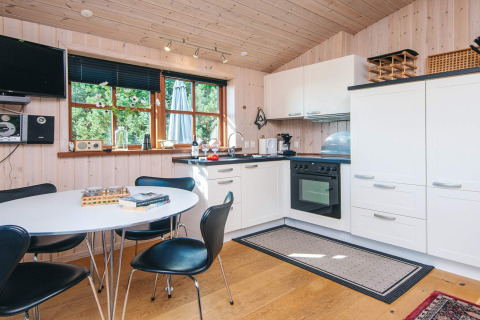 Cocina de madera luminosa con comedor, electrodomésticos modernos y ventana al verde en Ho Bay, Dinamarca.