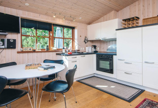 Cocina de madera luminosa con comedor, electrodomésticos modernos y ventana al verde en Ho Bay, Dinamarca.