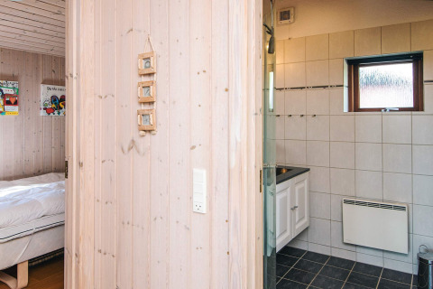 Blick vom Flur ins Badezimmer und Schlafzimmer einer holzvertäfelten Hütte, Seaside Escape in Ho Bay, Dänemark.