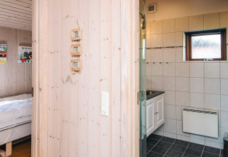 Blick vom Flur ins Badezimmer und Schlafzimmer einer holzvertäfelten Hütte, Seaside Escape in Ho Bay, Dänemark.