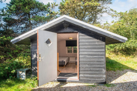 Sort træhytte med åben dør og udsigt til seng, omgivet af træer ved Seaside Escape i Ho Bugt, Danmark.