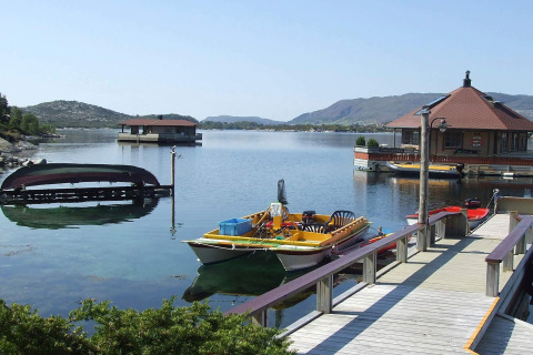 Foto de la casa flotante 38508-FISKHOLMEN con barcos en agua tranquila y montañas al fondo en Dinamarca.