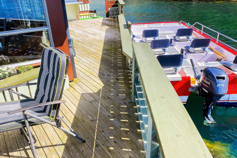 Escena de terraza con silla y lancha junto a la casa flotante 38508-FISKHOLMEN en Dinamarca, día soleado.