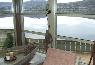 Vista desde la ventana de una casa flotante, mirando un lago y montañas, con velas y decoraciones delante.