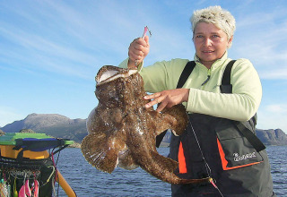Vrouw houdt grote vis vast, gevangen aan huisboot «38508-FISKHOLMEN» tijdens het vissen in Denemarken.