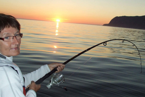 Mujer pescando desde la casa flotante «38508-FISKHOLMEN» en Dinamarca al atardecer con caña doblada.