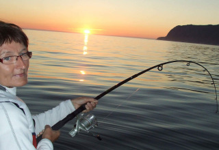 Mujer pescando desde la casa flotante «38508-FISKHOLMEN» en Dinamarca al atardecer con caña doblada.