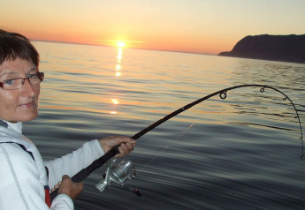 Vrouw vist van op woonboot «38508-FISKHOLMEN» in Denemarken bij zonsondergang, vishengel krom.