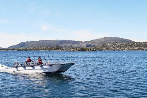 Dos personas navegan en una lancha cerca de Fiskholmen, Dinamarca, con montañas al fondo.