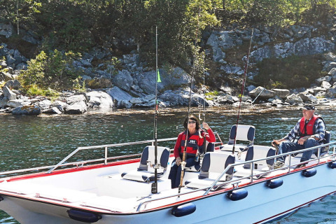 Dos personas pescando desde la casa flotante 38508-FISKHOLMEN en aguas tranquilas, cerca de una ribera rocosa en Dinamarca.