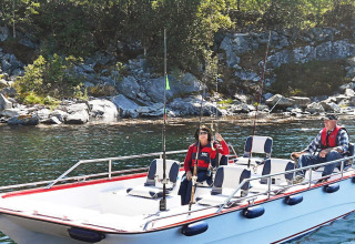 Twee personen vissen vanop de woonboot 38508-FISKHOLMEN, nabij een rotsachtige kustlijn in Denemarken.