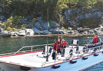 Twee personen vissen vanop de woonboot 38508-FISKHOLMEN, nabij een rotsachtige kustlijn in Denemarken.