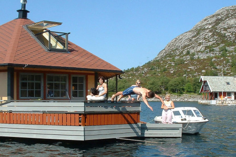 People relaxing on the houseboat 38507-SJØSTJERNEN in Denmark while a man dives into the water.
