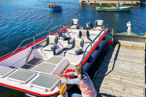 A person secures a boat to the dock at houseboat “38507-SJØSTJERNEN” in Denmark, with rowboats nearby.