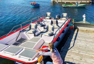 A person secures a boat to the dock at houseboat “38507-SJØSTJERNEN” in Denmark, with rowboats nearby.