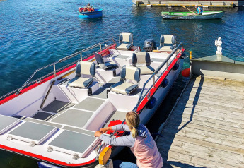 A person secures a boat to the dock at houseboat “38507-SJØSTJERNEN” in Denmark, with rowboats nearby.