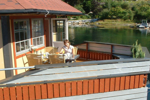 Woman dining on the deck of houseboat «38507-SJØSTJERNEN» in Denmark, overlooking calm water.