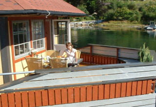 Woman dining on the deck of houseboat «38507-SJØSTJERNEN» in Denmark, overlooking calm water.