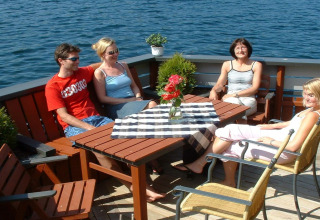 Four people enjoy the sun on a houseboat in Denmark, sitting around an outdoor table by the water.