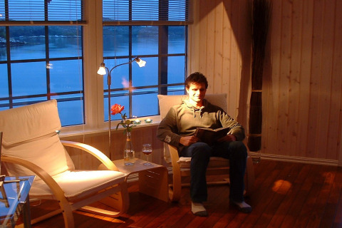 Man reading in a cozy living room with water view aboard houseboat 38507-SJØSTJERNEN in Denmark.