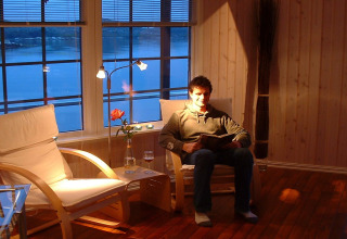 Man reading in a cozy living room with water view aboard houseboat 38507-SJØSTJERNEN in Denmark.