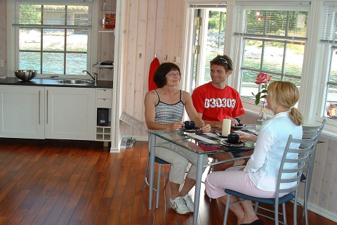 Three people sit at a glass table in the bright kitchen of houseboat 38507-SJØSTJERNEN in Denmark.