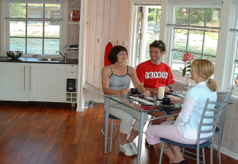 Three people sit at a glass table in the bright kitchen of houseboat 38507-SJØSTJERNEN in Denmark.