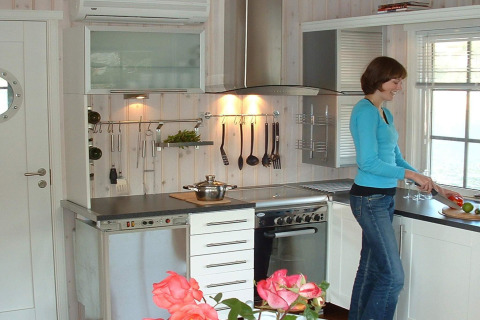 Woman cooking in the modern kitchen of houseboat 38507-SJØSTJERNEN, docked in Denmark.