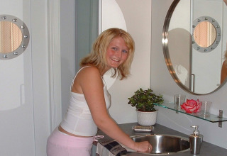 Woman smiling at sink in modern bathroom on houseboat ‘38507-SJØSTJERNEN’ in Denmark, with mirror and plant.