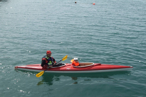 A person and a small dog wearing life jackets paddle a red kayak near houseboat 38507-SJØSTJERNEN in Denmark.