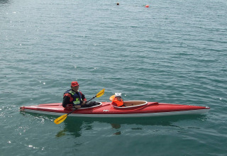 A person and a small dog wearing life jackets paddle a red kayak near houseboat 38507-SJØSTJERNEN in Denmark.